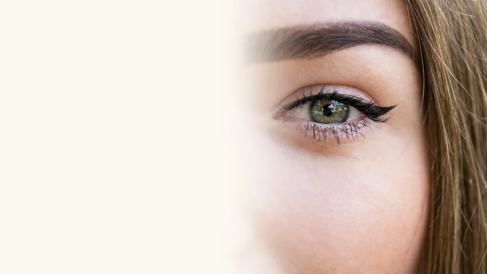 Close up of a woman's green eye with defined black winged eyeliner, a softly shaped brow and natural skin texture